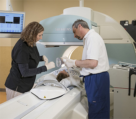 Two rad techs hooking patient up to Siemens nuclear medicine diagnostic imaging equipment